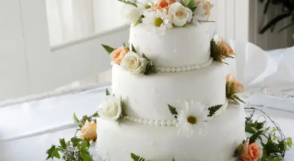 Elegancki tort weselny z białymi i brzoskwiniowymi różami, ozdobiony zielenią. Dowiedz się, jak zabezpieczyć kwiaty do tortu, by wyglądał pięknie.