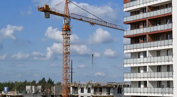 Plac budowy z dźwigiem i budynkami mieszkalnymi w tle.
