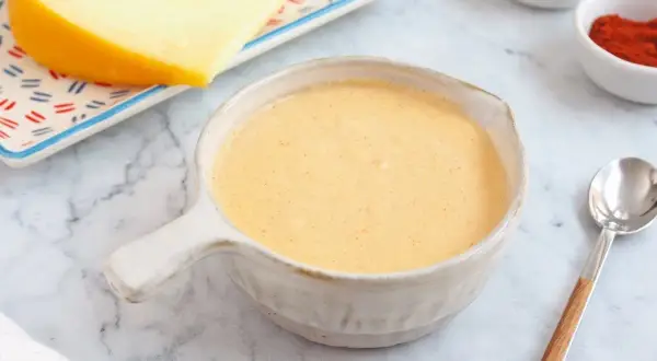 Crema de salsa de queso lista para servir, con un trozo de queso y especias al fondo.