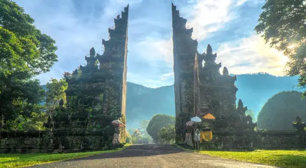 Brama na Bali, porośnięta mchem, zaprasza do podróży. Słońce wschodzi nad górami, a mgła otula krajobraz.