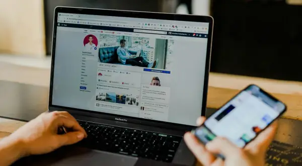 Osoba przegląda profil na Facebooku na laptopie, szukając informacji, jak usunąć znajomego na FB. Obok leży smartfon.