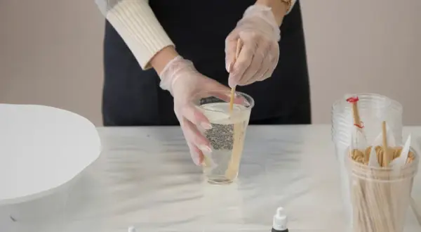 Mani guantate mescolano resina epossidica in un bicchiere, un passo fondamentale per imparare come usare la resina epossidica sul legno per creare opere d'arte uniche.