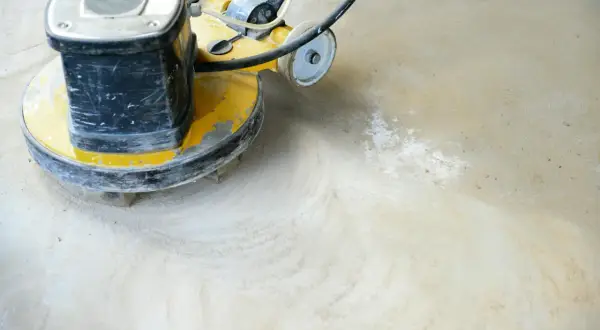Maschine schleift Beton. Staub wirbelt auf, während die rotierende Scheibe den Boden glättet.