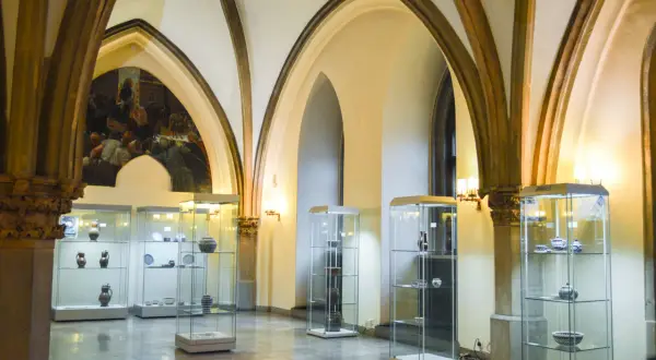 Wnętrze muzeum sztuki mieszczańskiej we Wrocławiu. W salach z arkadowymi sklepieniami wyeksponowano ceramikę i naczynia w szklanych gablotach.