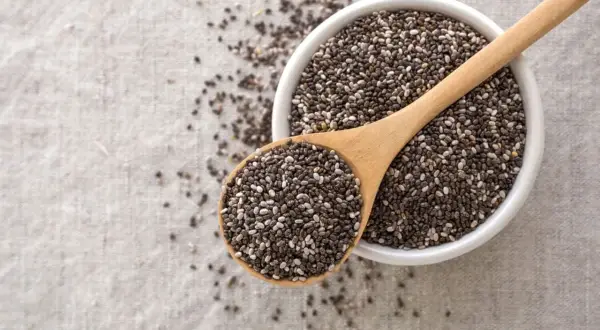 Semi di chia in una ciotola e cucchiaio di legno, un aiuto naturale per sgonfiare la pancia.