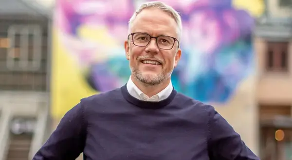 Niclas Hermansson ler glatt framför en färgglad väggmålning.