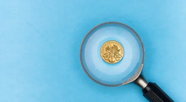 Złota moneta z instrumentami muzycznymi pod lupą. Próby złota widać na jej powierzchni.