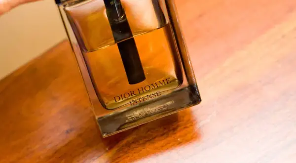 Elegancka butelka Dior Homme Intense z bursztynowym płynem na drewnianym blacie.