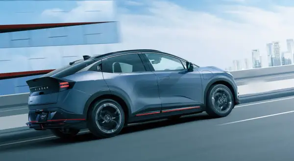 En blå Nissan Leaf 2026 glider fram på en motorväg med en stadssilhuett i bakgrunden.