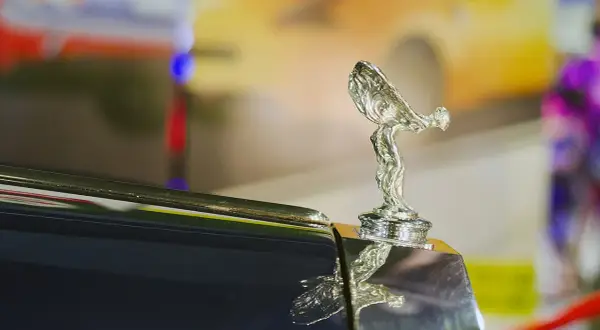 Den ikoniska Rolls-Royce kylarprydnad, "Spirit of Ecstasy", glänser på en mörk bil.
