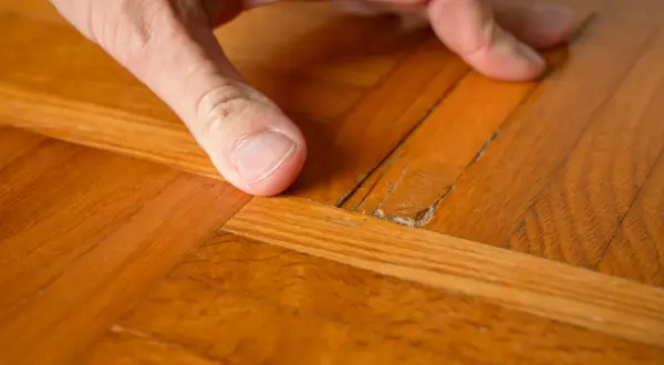 Dito come togliere la cera dal parquet verniciato: un dito indica una crepa sul legno lucido, mostrando il problema.