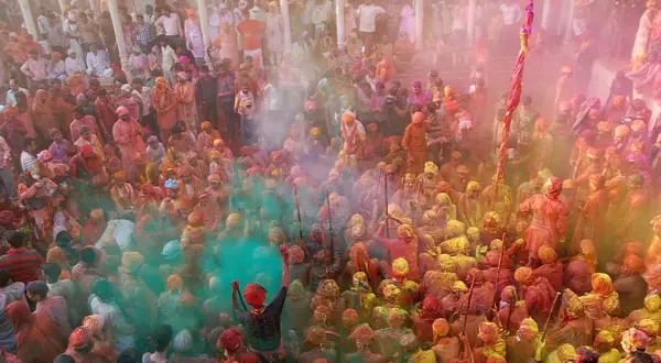 Tłum ludzi w kolorowych strojach, obsypany proszkami podczas święta Holi w Indiach.