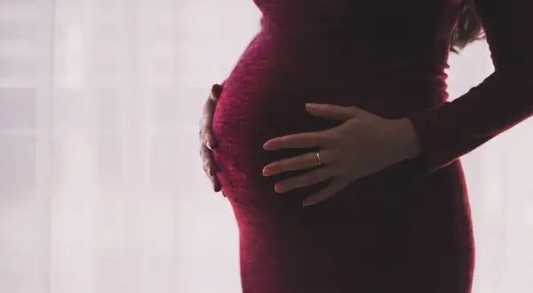 Ciężarna kobieta w czerwonej sukience obejmuje brzuch. Dylematy związane z umową zlecenie a ciążą.