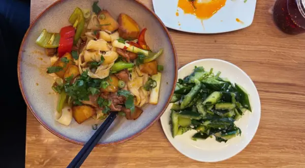 Ein Teller mit Nudeln, Kartoffeln und Gemüse, daneben ein Schälchen mit Gurkensalat. Typisch chinesisches Essen, das zum Genießen einlädt.