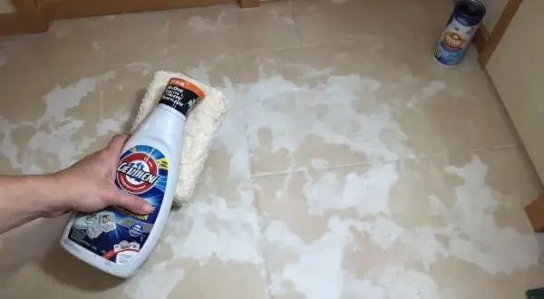 Main tenant nettoie carrelage neuf qui laisse un voile blanc avec un produit et une éponge.