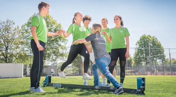 Junge Menschen üben auf einem Slackline-Parcours. Eine Dozentin unterstützt sie bei der physiotherapeutischen Ausbildung nebenberuflich.