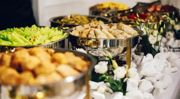 Stół z cateringiem: naleśniki, sałatka, smażone przekąski, dekoracje z kwiatów i białych kamieni.