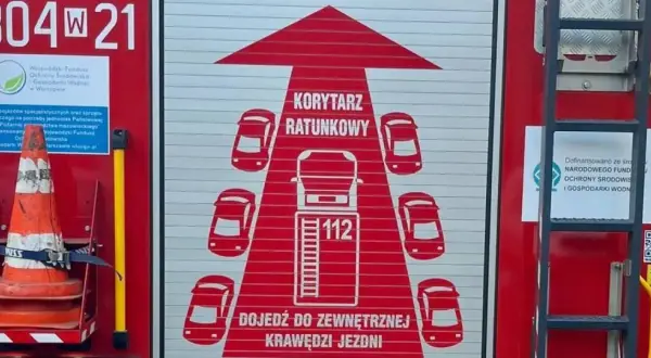 Grafika na drzwiach wozu strażackiego przedstawia korytarz życia, symbolizujący drogę dla pojazdów ratunkowych.