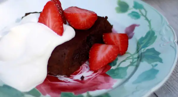 En bit fransk chokladtårta med vispgrädde och färska jordgubbar på en vacker tallrik med blomstermönster.