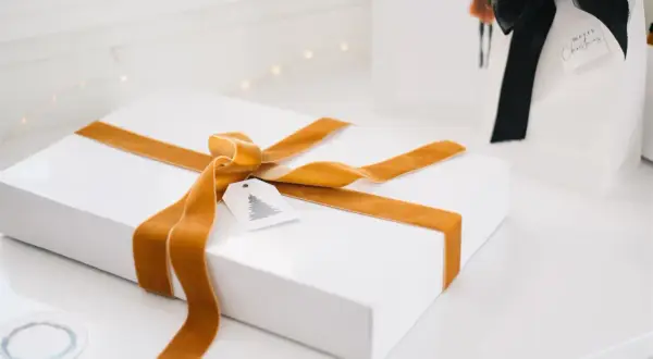 Ett vitt paket med gyllene sammetsband, ett sätt att slå in paket utan tejp. En julklapp med en liten etikett med gran.