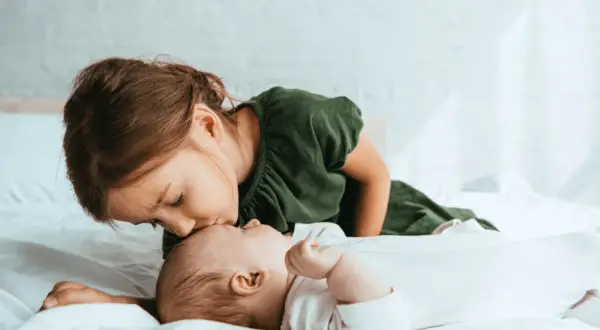 Starsza siostra czule całuje niemowlę w czoło. To uroczy obrazek, który może przypominać syndrom najstarszego dziecka, gdy przejmuje opiekę.