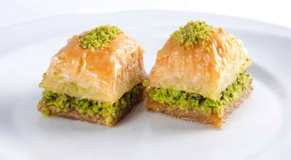 Zwei süße, schichtweise gebackene Teigstücke mit Pistazienfüllung und Sirup. Das ist Baklava, ein köstliches Dessert.