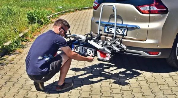 Mężczyzna montuje dodatkową tablicę rejestracyjną na bagażniku rowerowym.