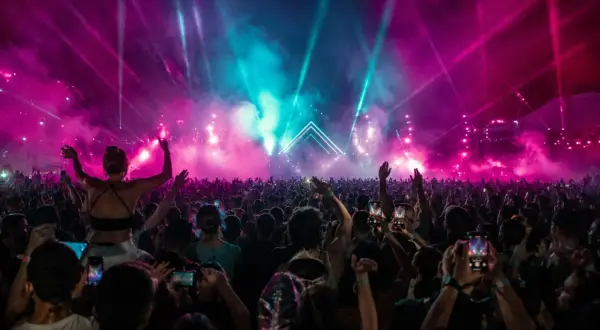 Ein riesiges Publikum feiert unter psychedelischen Lichteffekten und Nebel. Die Stimmung ist wie bei einem **psychedelic circus**.