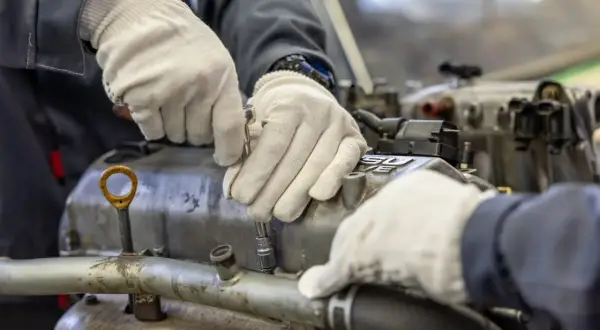 Mechanik w białych rękawiczkach dokręca śrubę na silniku, pracując nad jego cylindrem.