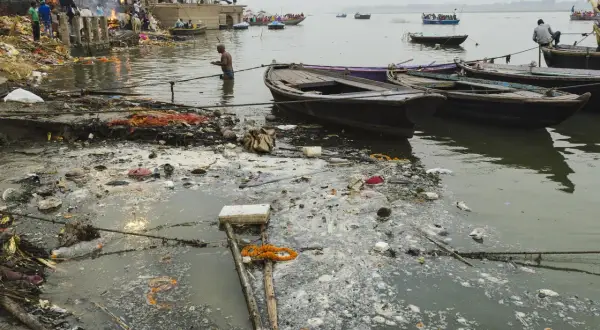Rzeka Ganges, święta w hinduizmie, jest miejscem rytuałów i kremacji. Widać łodzie i ludzi na brzegu, ale też śmieci unoszące się na wodzie.