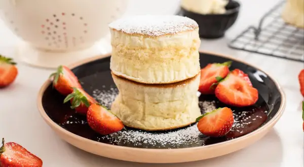 Två fluffiga amerikanska pannkakor staplade på en tallrik med färska jordgubbar och pudersocker.