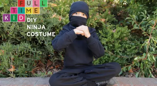 Dziecko w czarnym stroju ninja siedzi na ziemi, ręce złożone w geście.