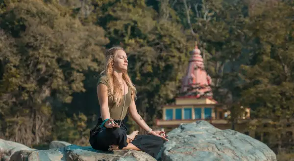 Mujer meditando en postura de loto sobre rocas, con un templo al fondo. Un momento de paz y el despertar de la conciencia.