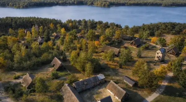 Wdzydze Kiszewskie: skansen z drewnianymi chatami i wiatrakiem nad jeziorem, otoczony jesiennym lasem.