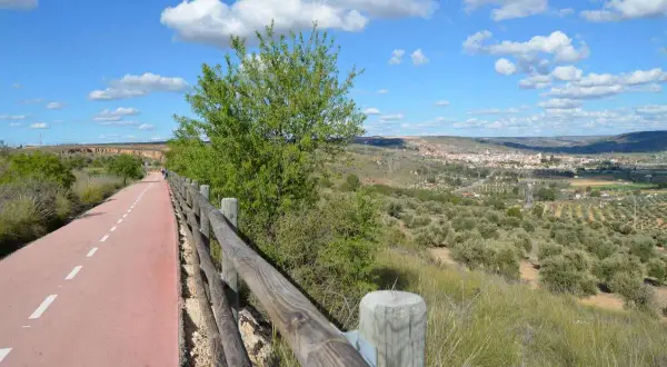 Un camino ciclista y peatonal, la **vía verde del Tajuña**, serpentea entre vegetación y un paisaje de olivos con un pueblo al fondo.