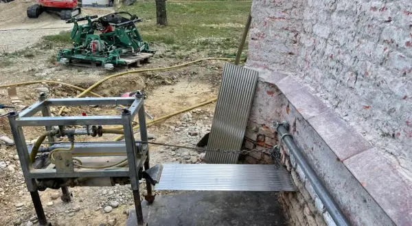 Baustelle mit Bagger, Maschine und Metallkonstruktion. Eine horizontale Sperrschicht aus Metallblech schützt die Ziegelwand.
