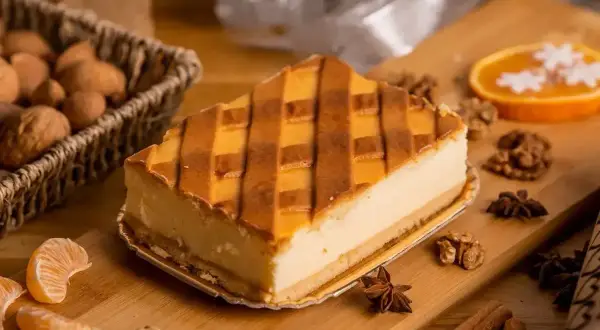 Kawałek sernika z kratką z kruchego ciasta, otoczony orzechami, mandarynkami i przyprawami.