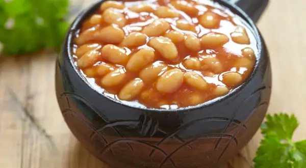 Un bol de haricot blanc en sauce tomate, garni de persil frais, sur fond de bois.