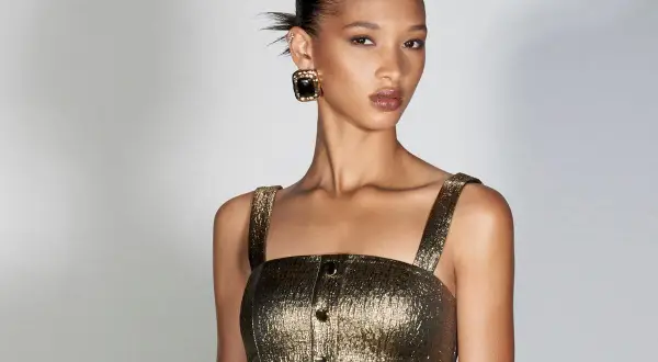 Modella con bronzer come si usa per un look radioso. Capelli raccolti, top dorato e orecchini neri.
