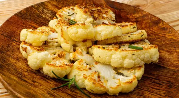 Tranches de chou-fleur entier au four, dorées et savoureuses, garnies de romarin frais sur une assiette en bois.