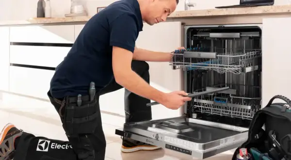 Serwisant w ubraniu z logo Electrolux naprawia zmywarkę. Electrolux to znana firma produkująca sprzęt AGD.