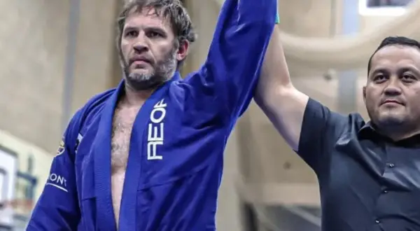 Tom Hardy i blå gi, med armen lyft som segrare i BJJ.