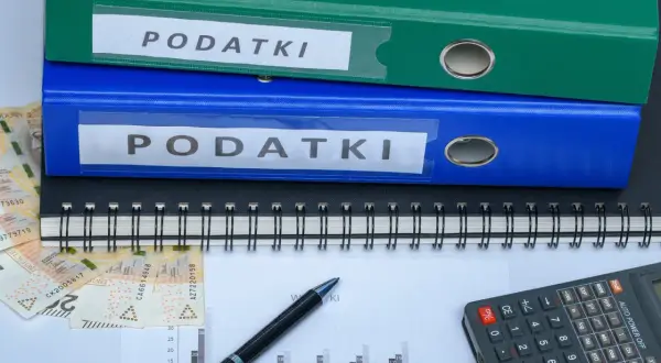 Segregator z napisem "PODATKI", pieniądze, kalkulator i wykres. Szukasz sposobu, jak zmniejszyć podatek za budynki gospodarcze?