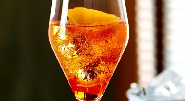 Ein Aperol Sour im Glas mit Eiswürfeln und Orangenzeste, Bläschen steigen auf.