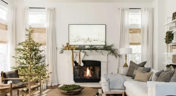 Cozy living room with a lit Christmas tree and fireplace, showcasing elegant holiday mantel ideas with stockings and greenery.