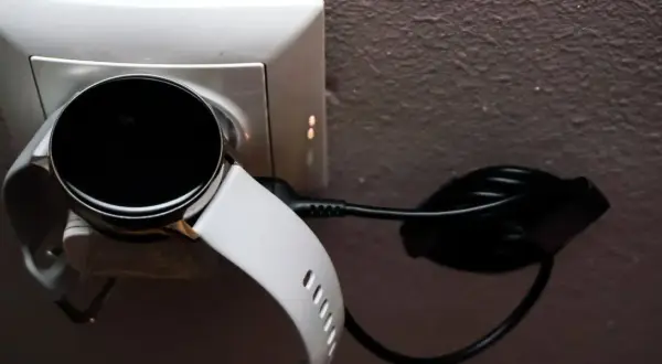 Biały smart bracelet podłączony do ładowarki w gniazdku. Dowiedz się, jak ładować swój smart bracelet.