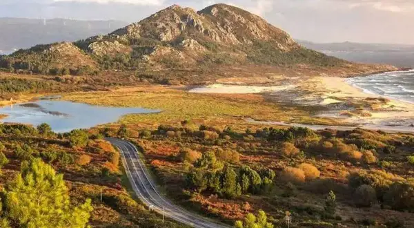 Carretera serpenteante hacia el monte Louro, con un lago, dunas y el mar al fondo.