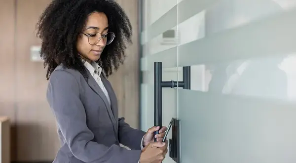 Donna con afro e occhiali usa lo smartphone per la rilevazione presenze, aprendo una porta in vetro.