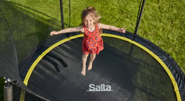 Ein fröhliches Mädchen springt auf einem Trampolin. Die Frage "Trampolin ab welchem Alter?" stellt sich hier nicht, denn Spaß kennt kein Alter!