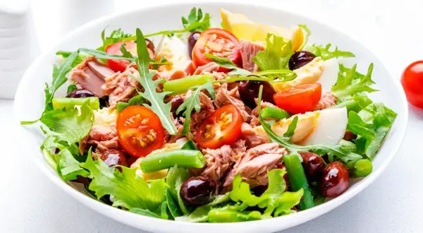En fräsch sallad nicoise med tonfisk, ägg, tomater, gröna bönor och oliver på en bädd av grönsallad.